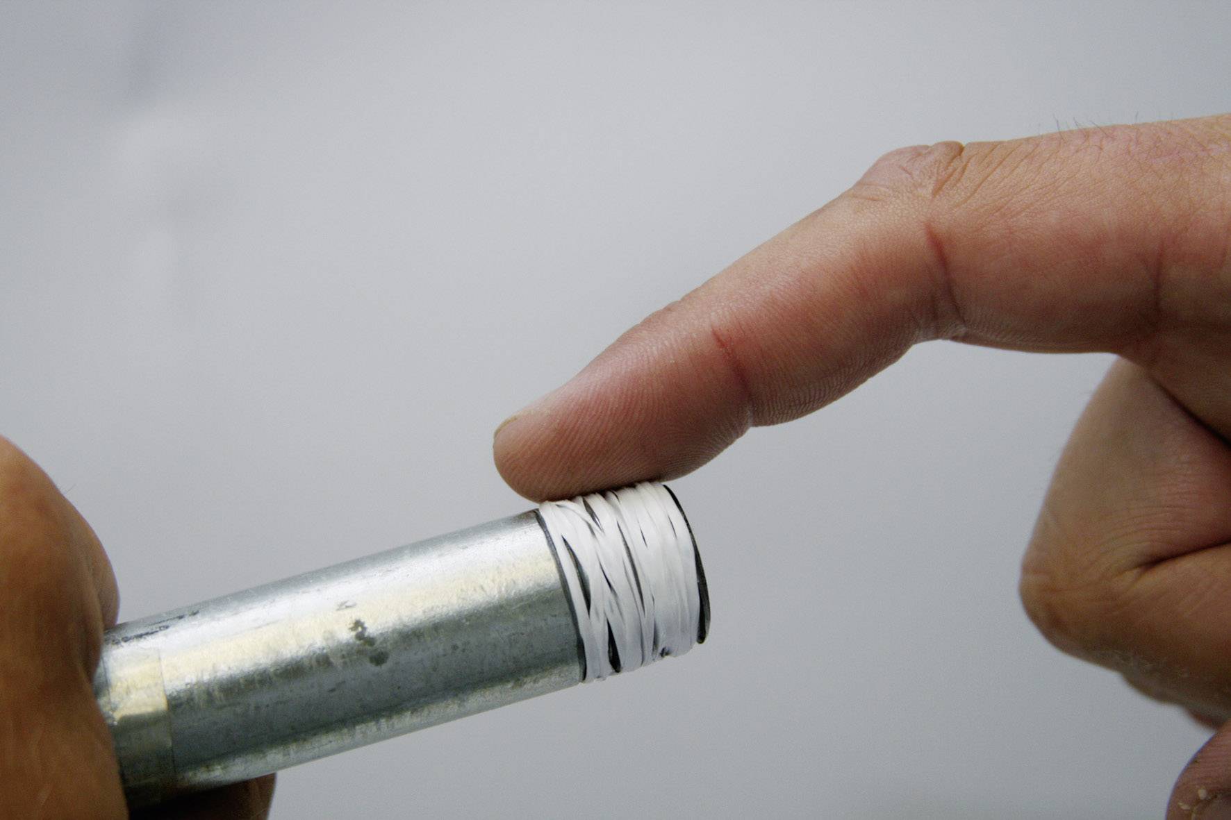 Ein Finger berührt das Ende eines Metallrohrs, das mit weißem Dichtungsband umwickelt ist. Fokus liegt auf der Anwendung und Dichtung.