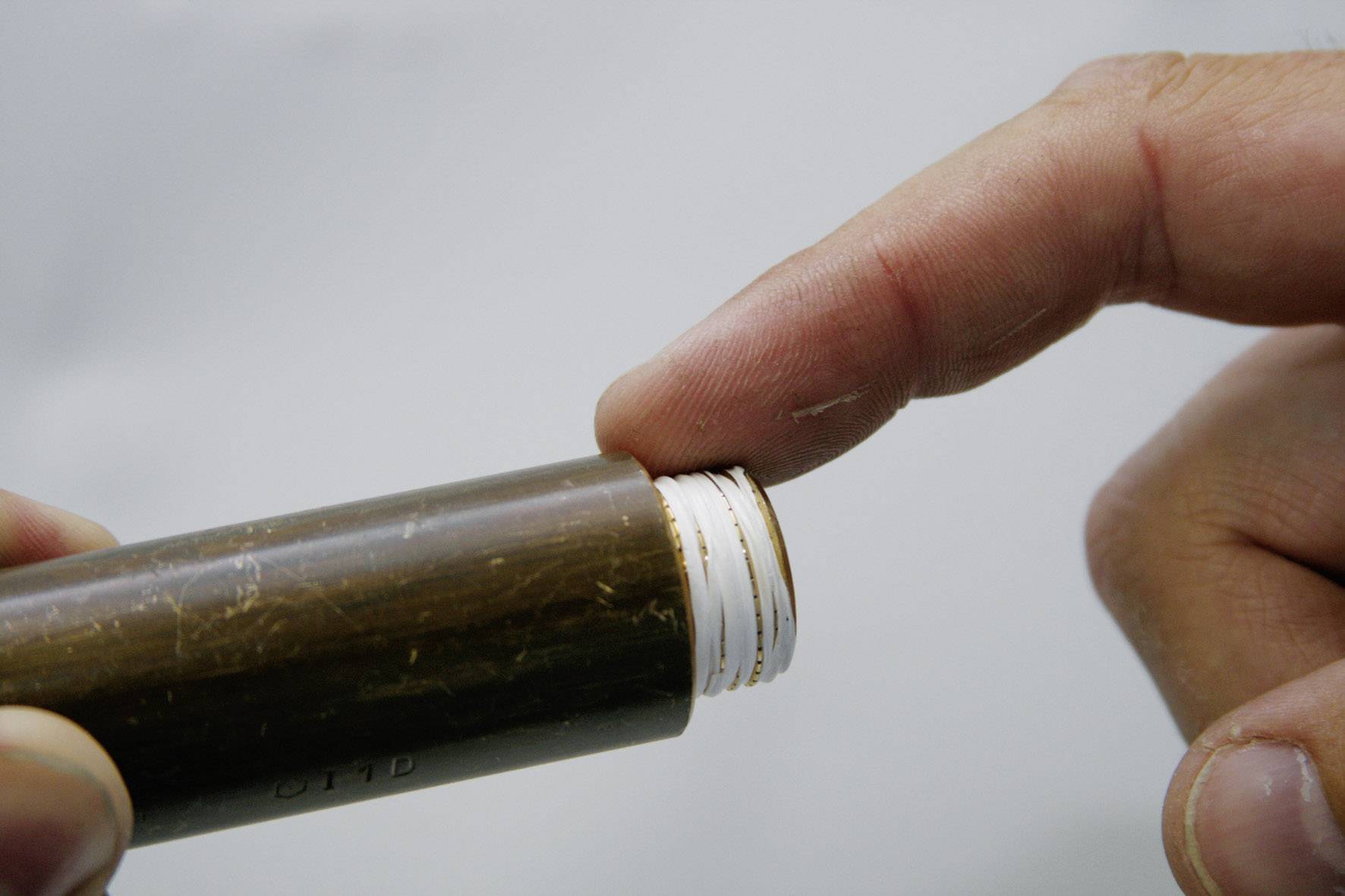 Eine Hand berührt den weißen Rand einer braunen Plastikröhre, möglicherweise, um eine Textur oder Funktion zu überprüfen.