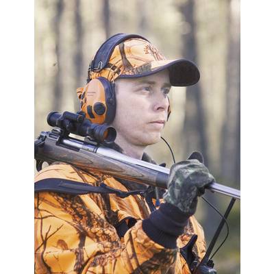 Eine Person in orangefarbener Jagdbekleidung trägt ein Gewehr und trägt Kopfhörer, während sie aufmerksam in einem bewaldeten Gebiet steht.