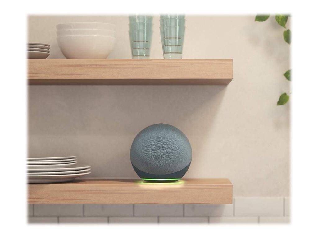 Ein grauer, kugelförmiger Smart Speaker leuchtet grün auf einem Holzregal.