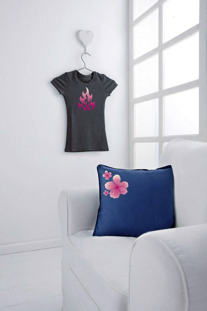 Ein graues T-Shirt mit pinkem Flammen-Logo hängt an der Wand. Auf dem weißen Sofa liegt ein blaues Kissen mit pinker Blume.
