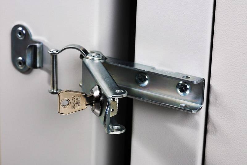 Ein Metallscharnier mit integriertem Schloss, an einer Tür befestigt. Ein Schlüssel steckt im Schloss.