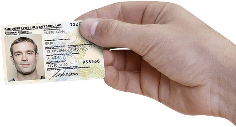 Eine Hand hält einen deutschen Personalausweis mit Foto, Namen 'Erik Mustermann', Geburtsdatum und Ausstellungsdetails rechts oben erkennbar.
