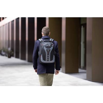 Eine Person mit einem Rucksack geht auf einem Bürgersteig entlang eines modernen Gebäudes.