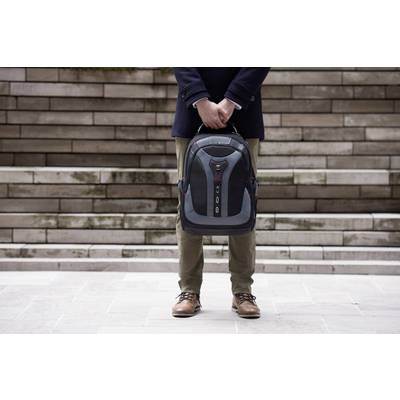 Eine Person hält einen Rucksack vor sich. Hintergrund mit Treppenstufen aus Stein. Die Person trägt braune Schuhe und einen dunklen Mantel.