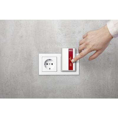 Hand drückt auf den Knopf eines WLAN-Repeaters, der neben einer Steckdose an einer grauen Wand installiert ist.