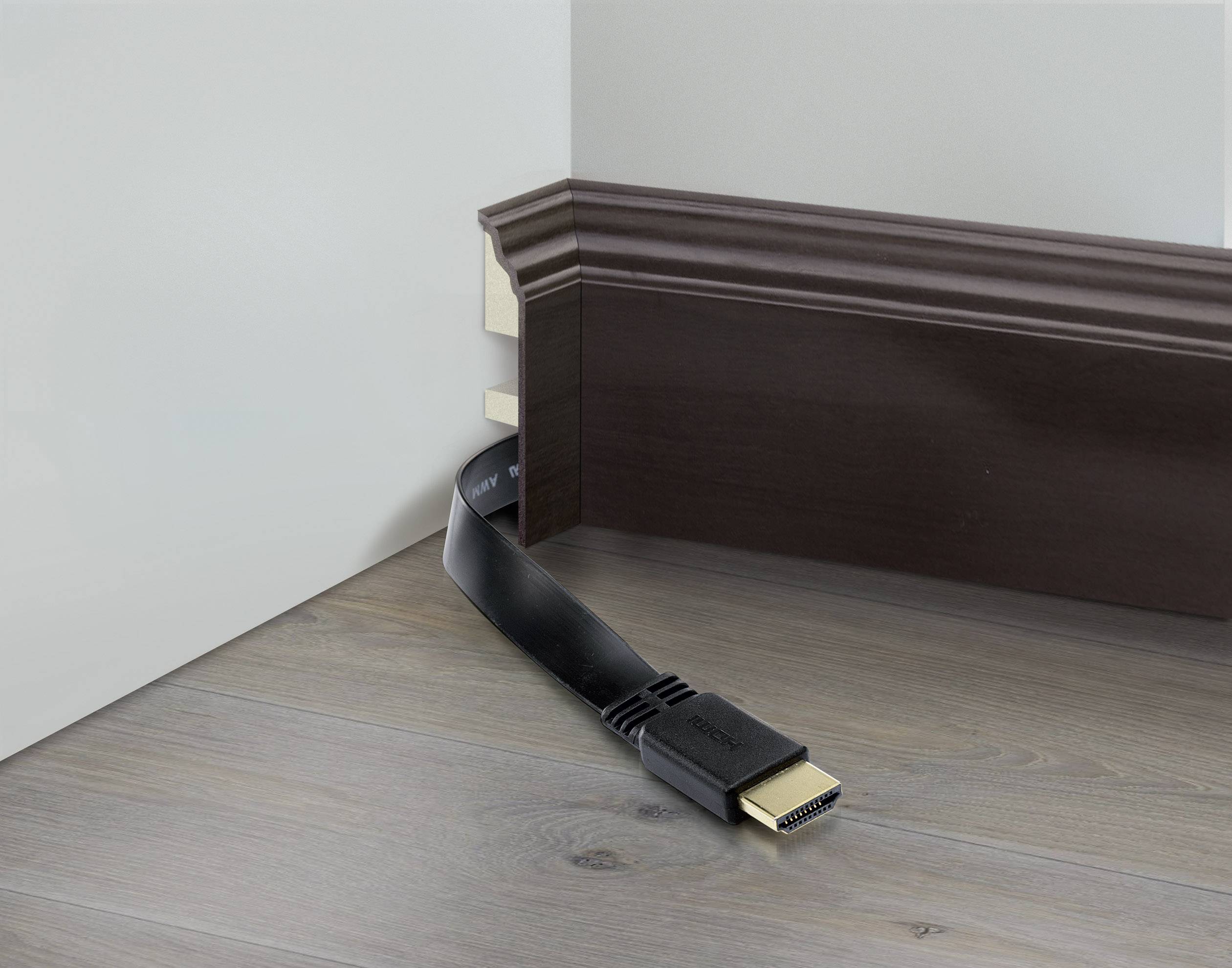 'Flaches HDMI-Kabel unter einer braunen Fußleiste versteckt, biegt um die Ecke zu hellem Holzboden.'