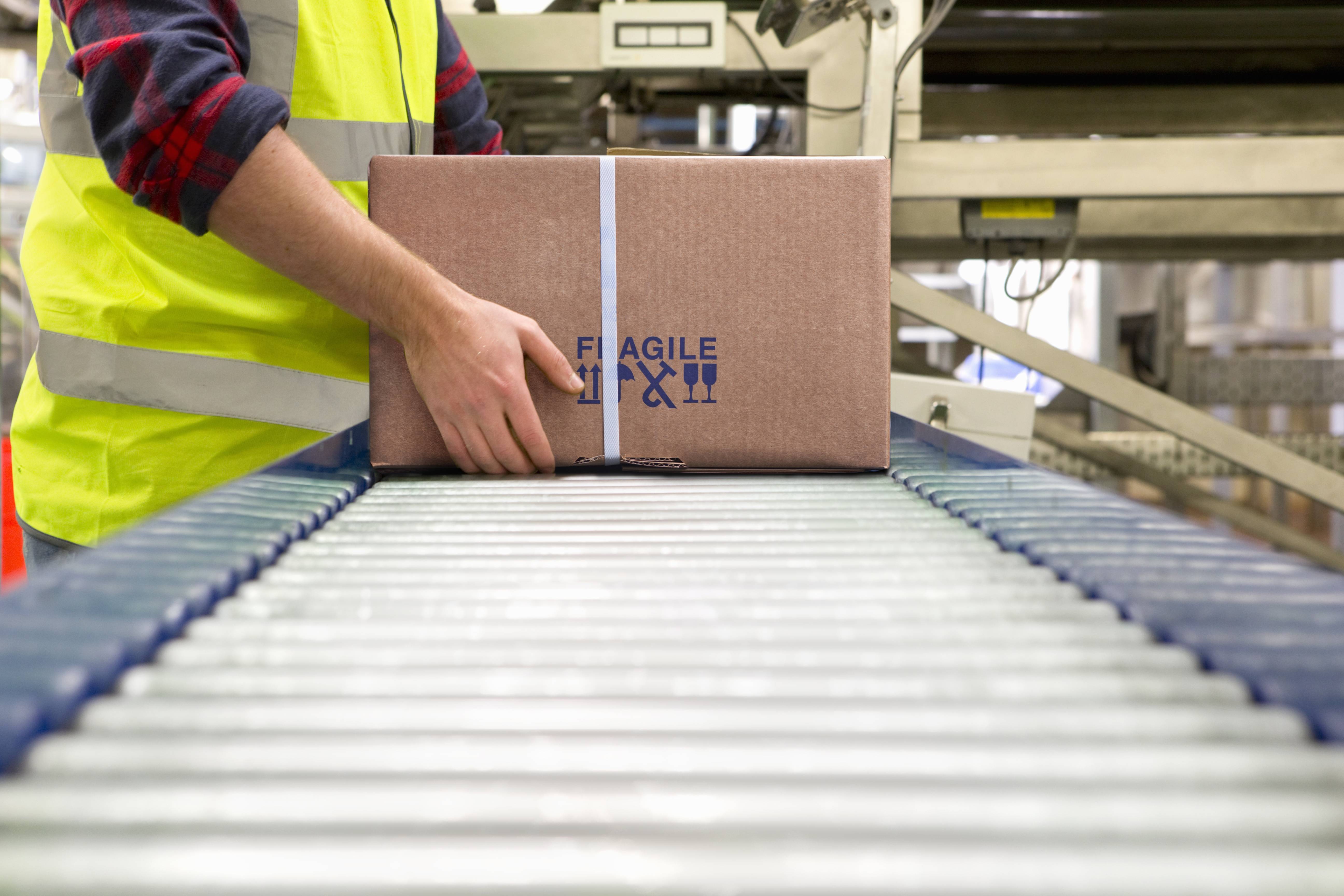 Ein Mitarbeiter in Warnweste platziert ein Paket auf einer Rollenbahn im Lager.