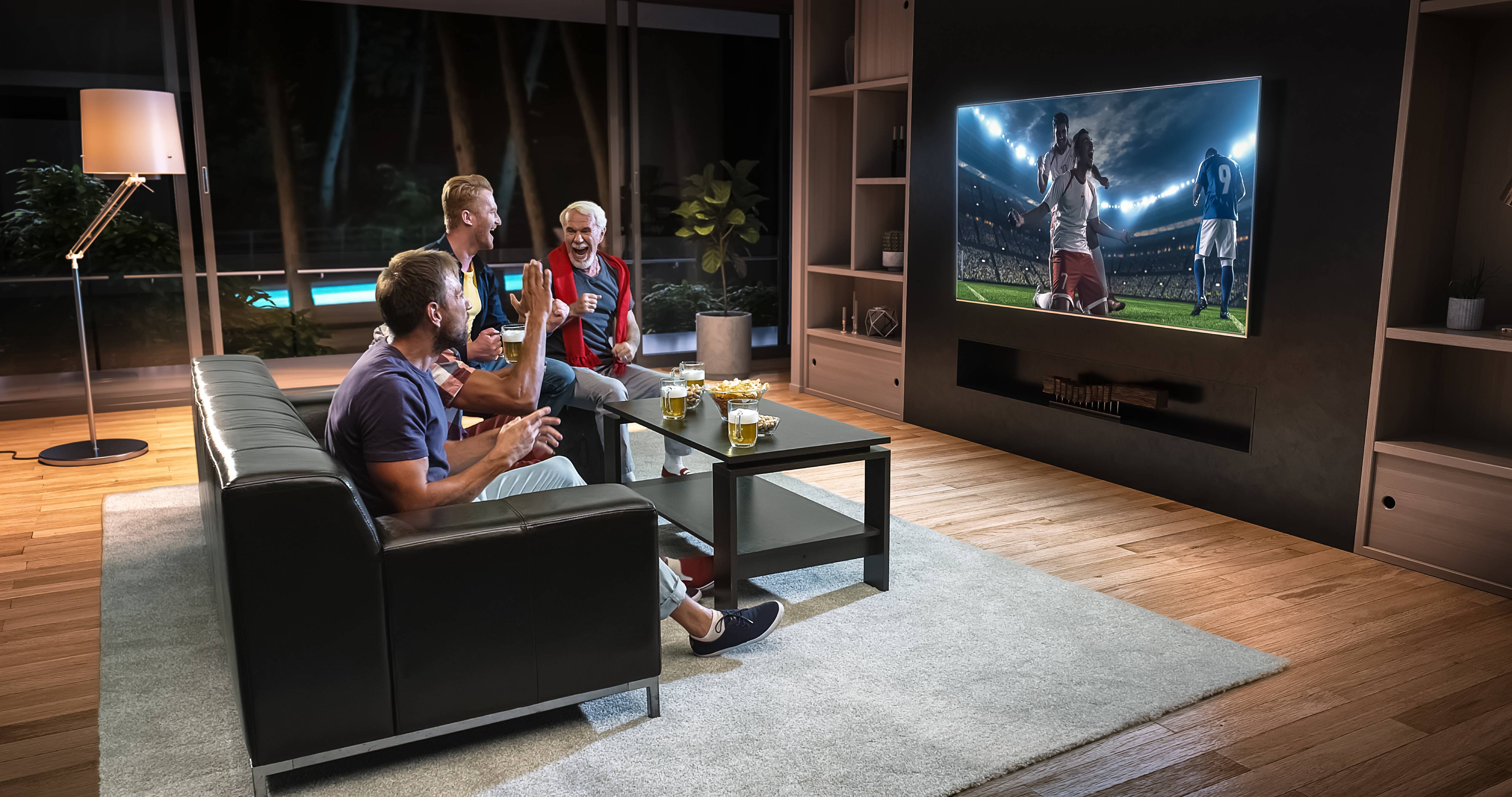 Vier Freunde sehen Fußball im Wohnzimmer. Smart Home Entertainment und Beleuchtung schaffen eine angenehme Atmosphäre.