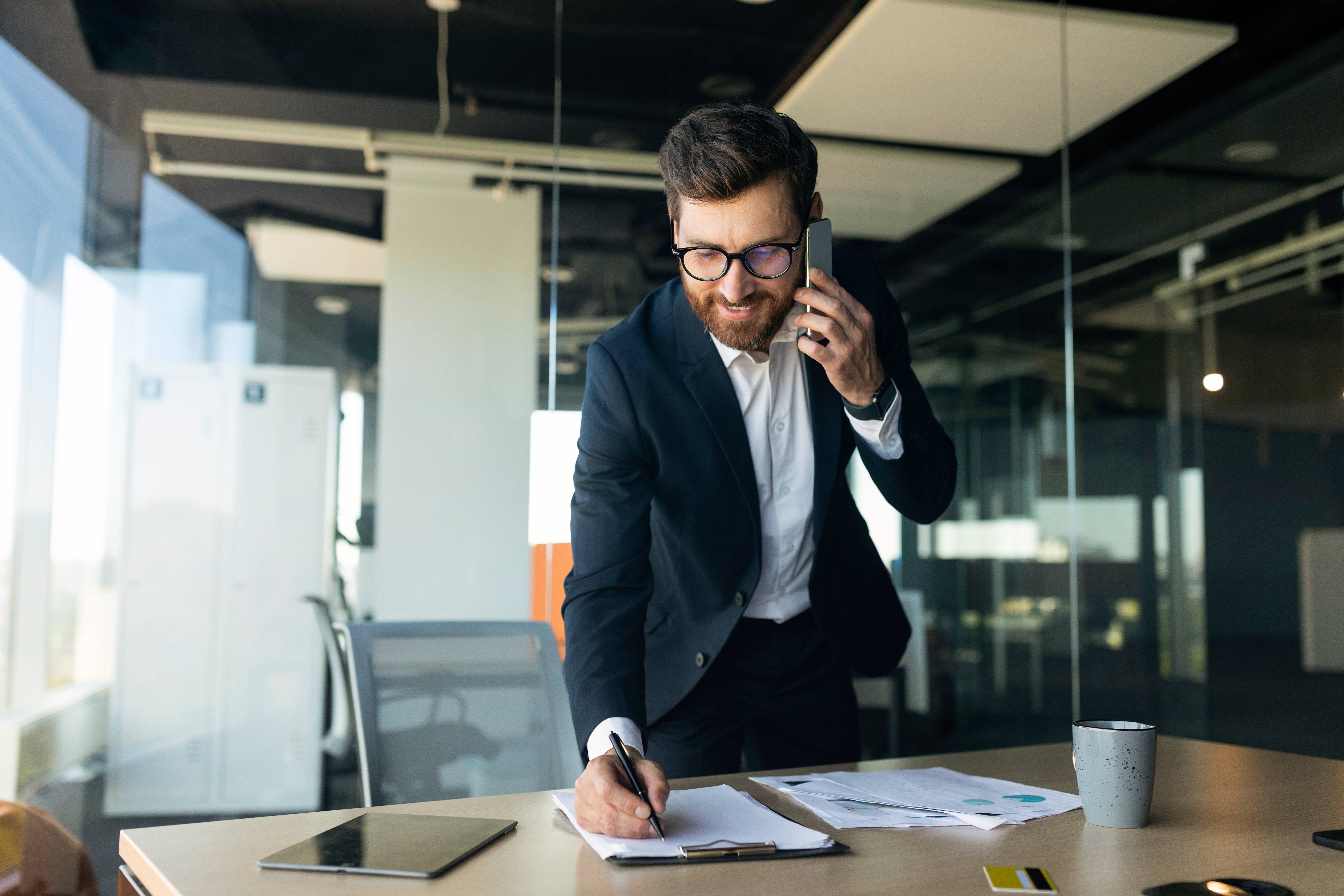 Das Bild zeigt einen Geschäftsmann, der mit einem Smartphone telefoniert und sich dabei Notizen macht.