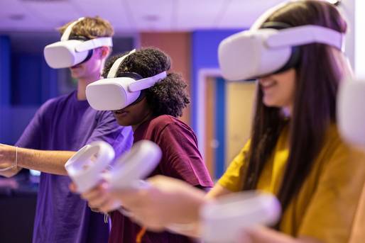 Junge Leute mit weißen VR-Brillen und Controllern tauchen in virtuelle Umgebung ein. 