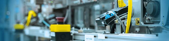 Nahaufnahme einer modernen industriellen Fertigungsstraße. Sensoren, gelbe Kabel und Steuerungskomponenten visualisieren die Automatisierung und Produktion.