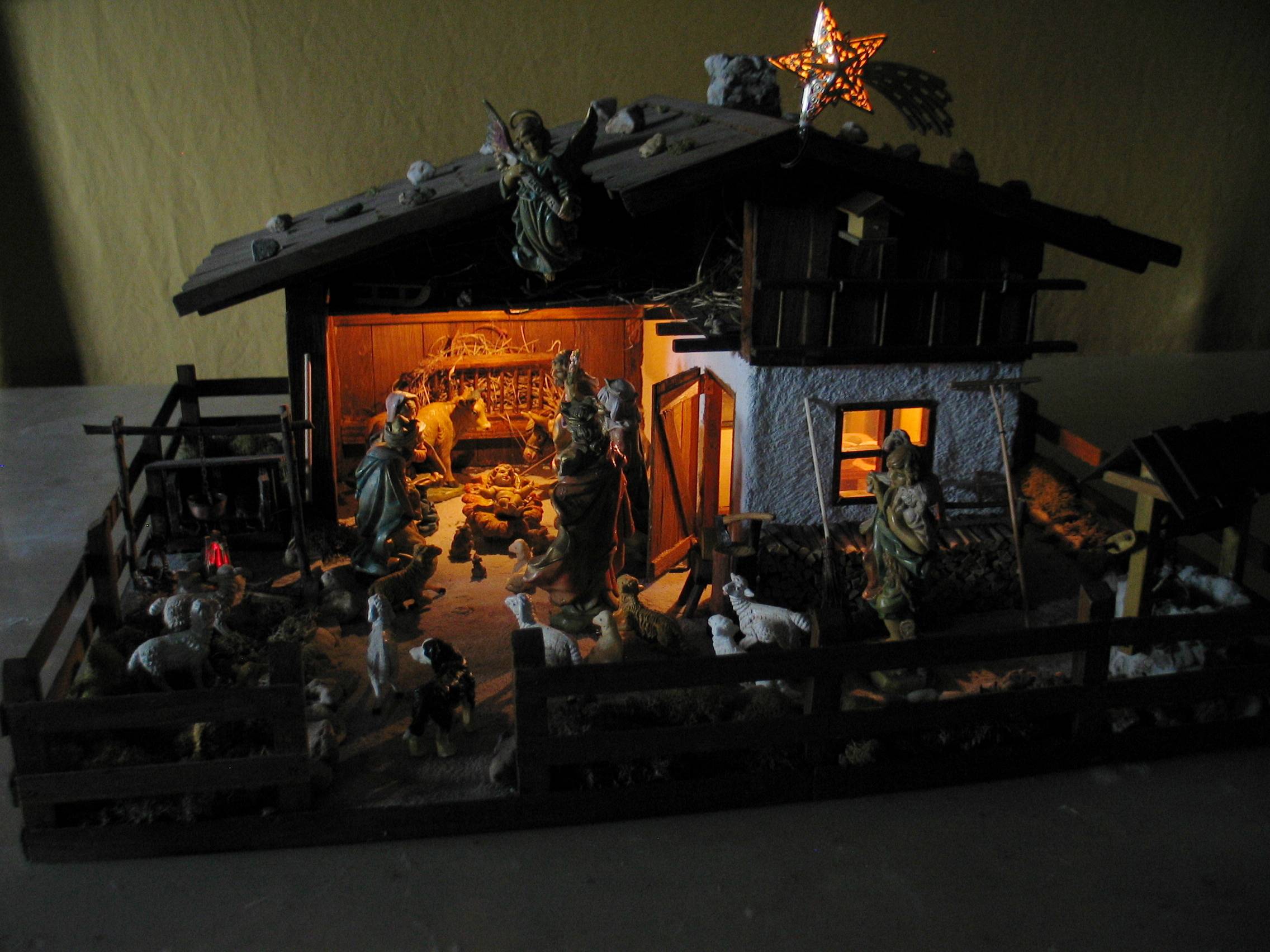 Das Bild zeigt die Weihnachtskrippe vom Titelbild bei Dunkelheit. Lediglich der Stallbereich mit den Figuren, der Innenraum und der Stern am Dach sind dezent mit warmweißem Licht beleuchtet.