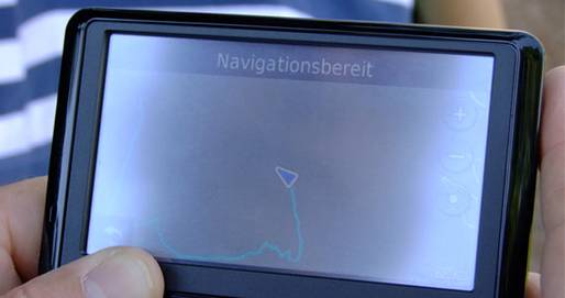 Das Bild zeigt ein GPS-Gerät in Großaufnahme, das jemand in seinen Händen hält. Auf dem Display ist zu sehen, dass der Besitzer/die Besitzerin schon einen längeren Weg zurückgelegt hat, es sind jedoch keine Kartendetails zu erkennen, da der Bildschirm das Licht stark spiegelt.