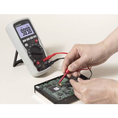 Someone is measuring the voltage on a computer circuit board using a multimeter. The multimeter is displaying 9.888 V.