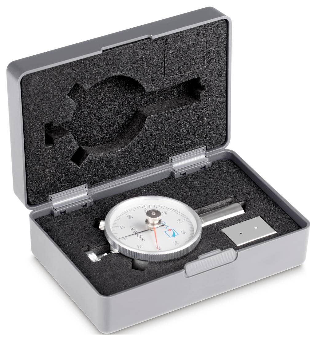 Analogue measuring instrument in an open box with foam insert and accessories. Main scale showing measurement values.