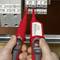 A person is holding two red voltage testers in front of a grey fuse box to measure electrical voltage.