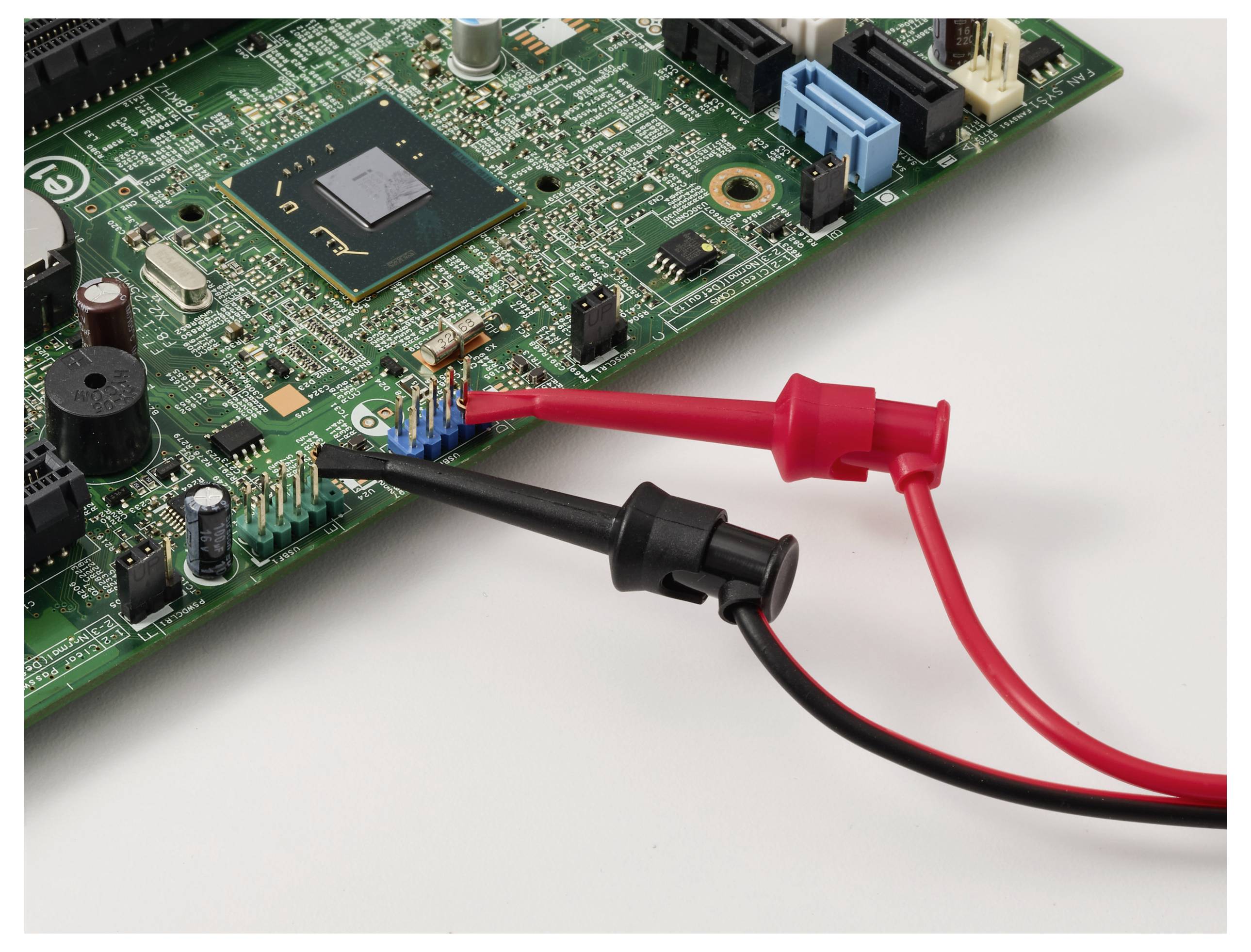 An electronic circuit board is being tested with a multimeter using red and black probes connected to different points.