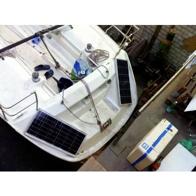 A sailing boat with two solar panels on the deck, moored in a workshop environment. Tools and materials are visible in the background.