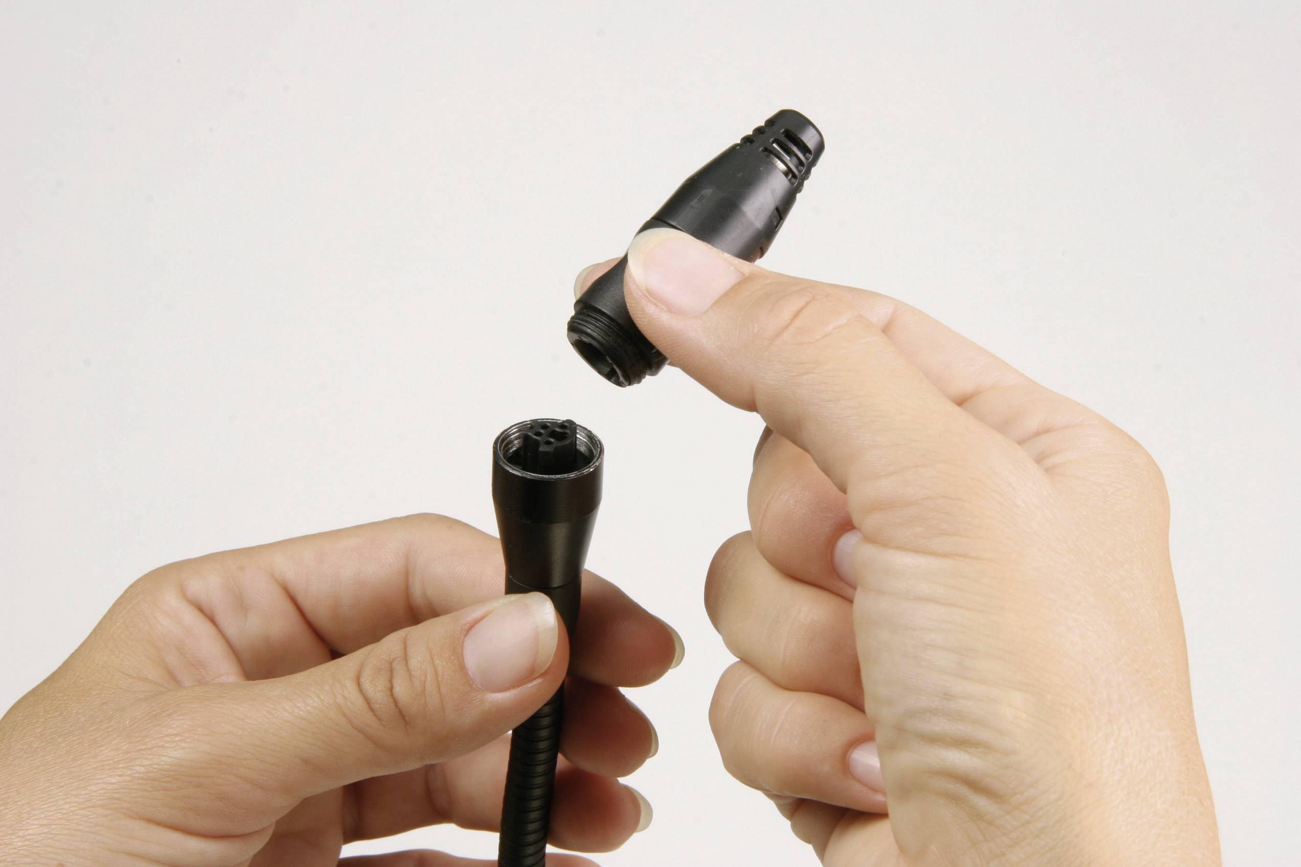 Two hands connect two black cable ends with each other.