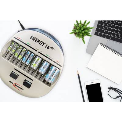 Battery charger with six AA batteries inserted, placed next to a laptop, a notebook, a mobile phone, and a small plant.