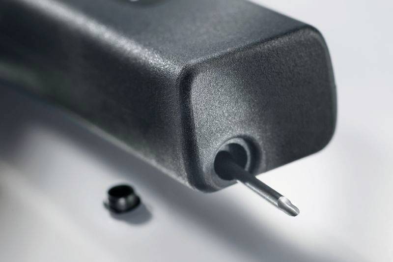 Close-up of a metal rod protruding from a black plastic casing. A small, round object is blurred in the background.