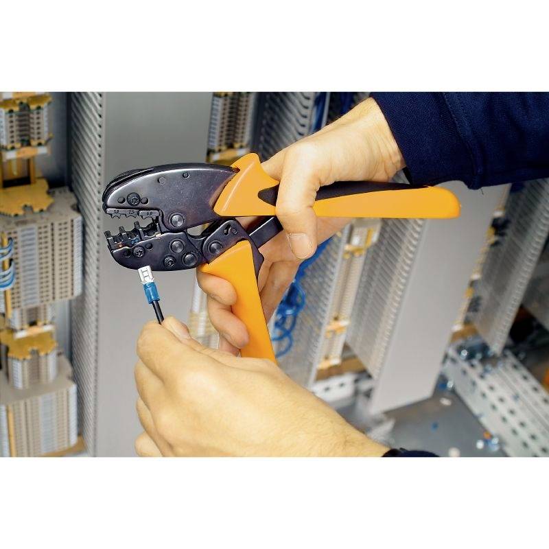A person is using an orange crimping tool to secure a cable lug onto a cable in an electrical cabinet.