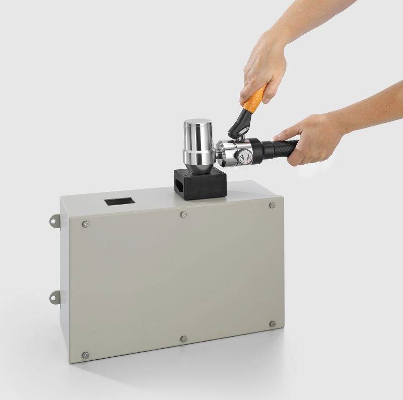'A person using a tool to adjust a metallic component on a large rectangular gray box against a plain background.'