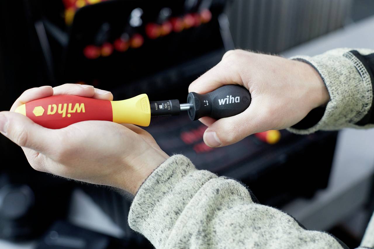 'Close-up of two hands holding a screwdriver with a red and yellow handle. Tools can be seen in the background.'
