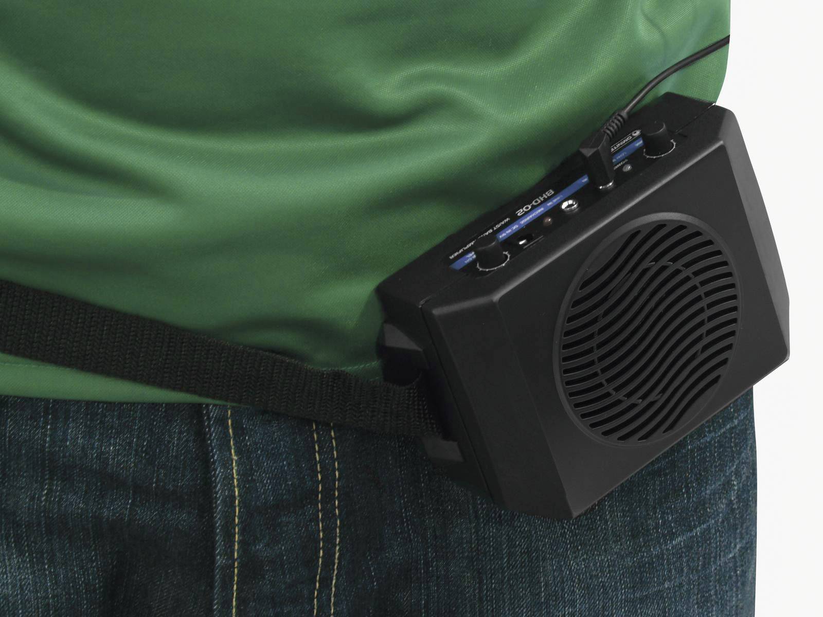 Portable speaker attached to a belt, worn by a person dressed in a green top and blue jeans.