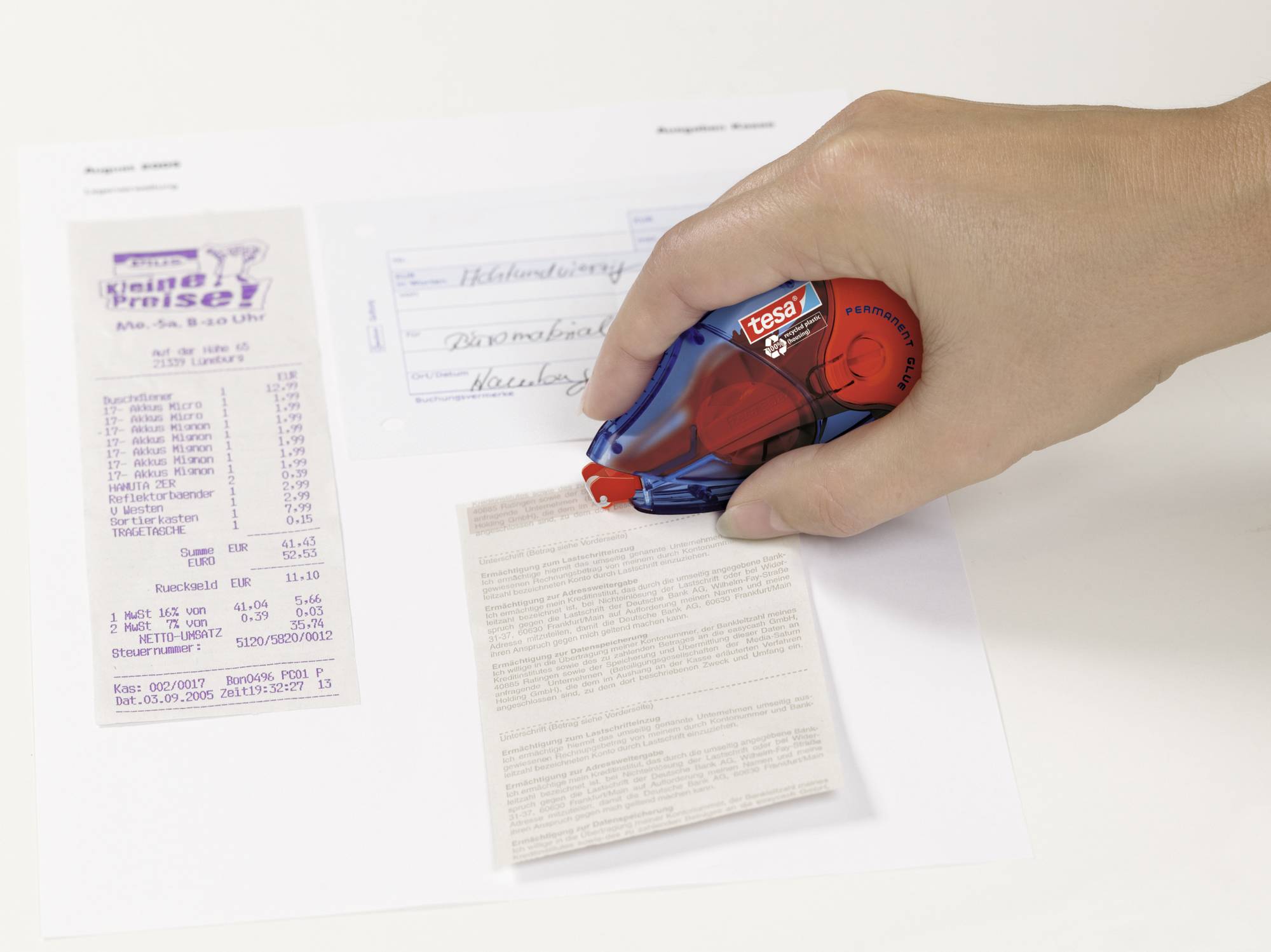 A hand is using a correction roller over a document on a table. Beside it lies a till receipt and a small envelope.