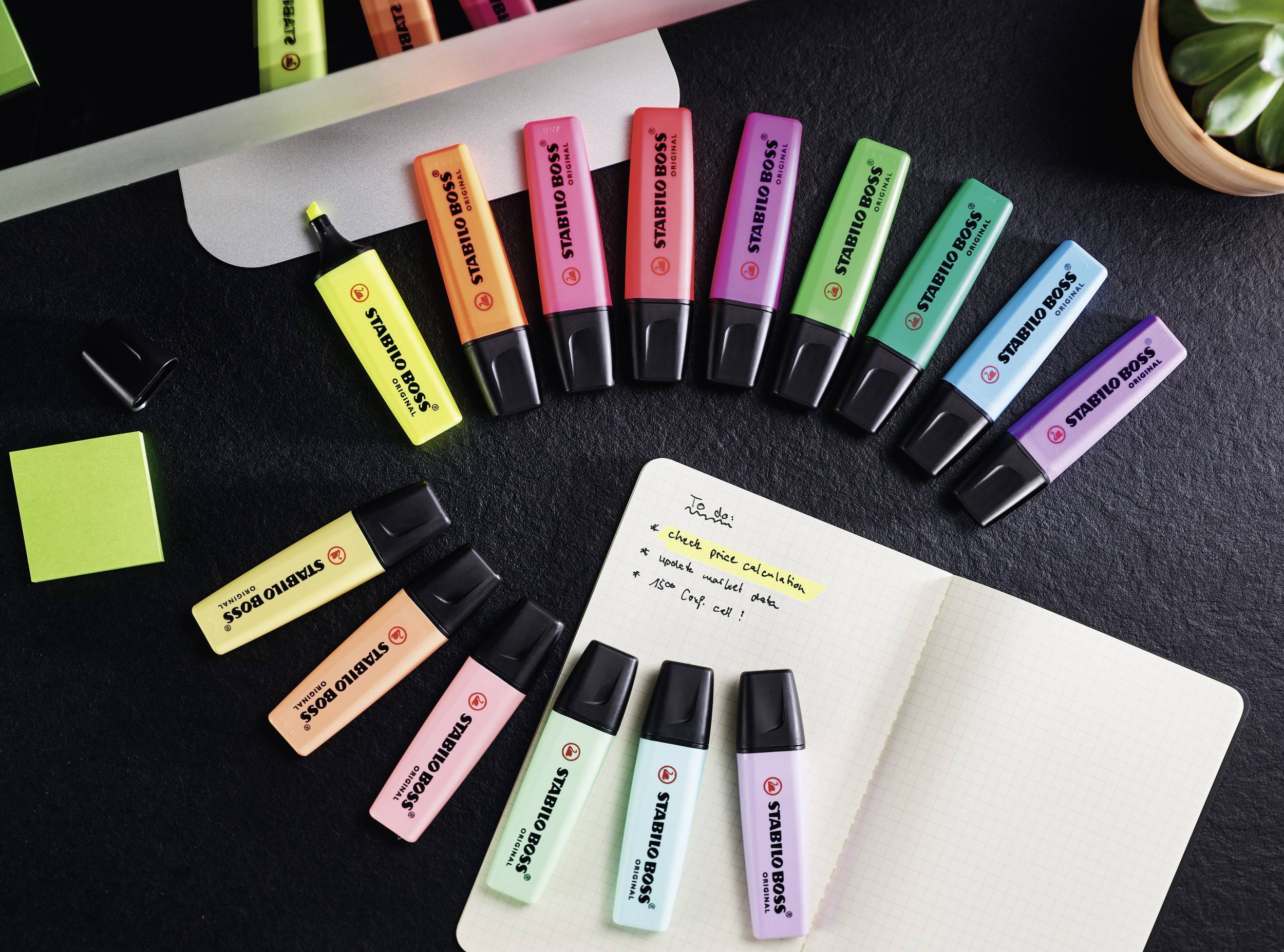 Highlighter pens in various colours are spread out fan-like on a table. A notebook displays handwritten notes in black ink.