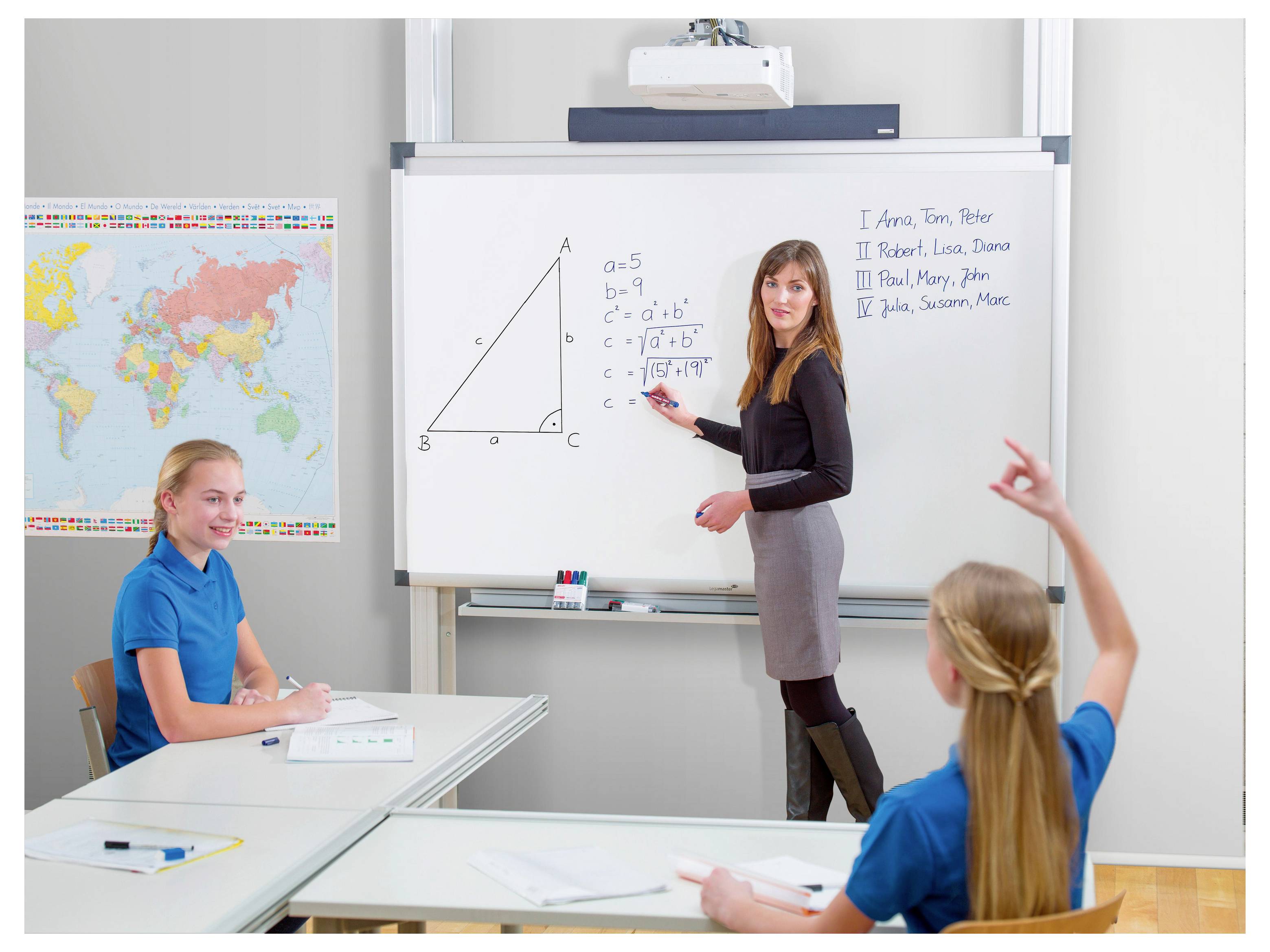 Teacher writing triangle calculations on a classroom whiteboard while students sit at desks and one raises a hand.