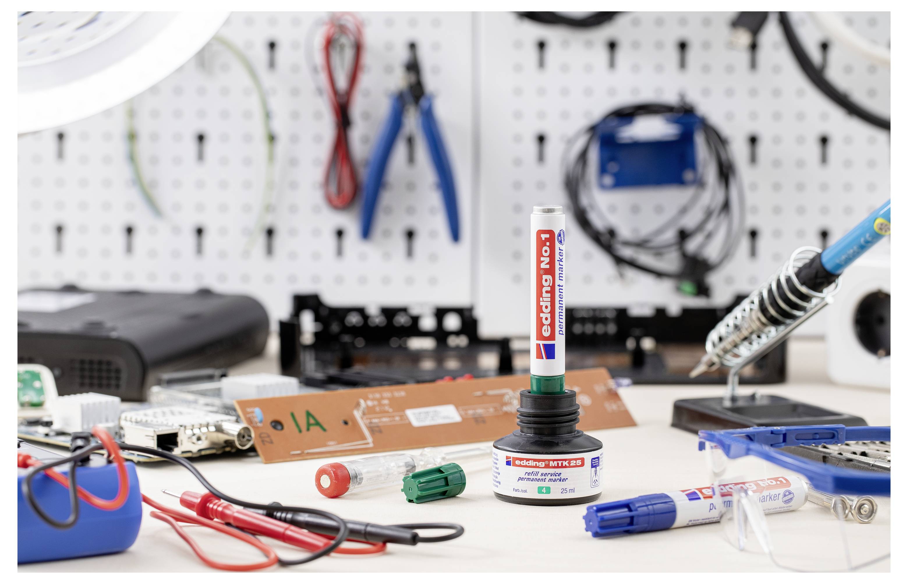 Electronics workbench with a soldering iron and tools, centered on a 'coding pen' standing in a holder, with circuit boards, wires, and components spread across the table.