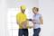 A delivery driver in a yellow shirt and cap hands a package to a woman. She is holding a clipboard and signing for the delivery.
