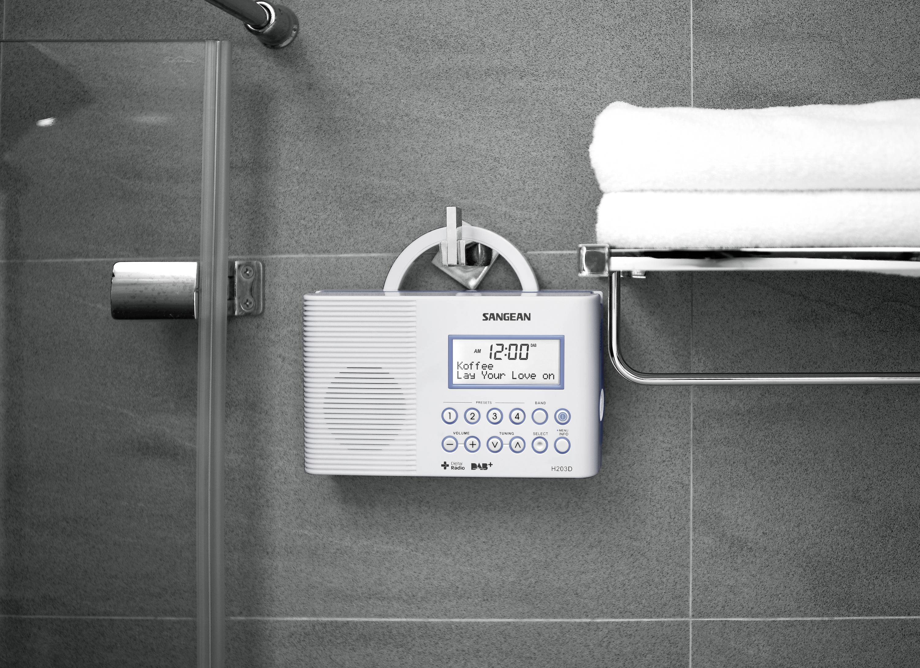 A portable radio is mounted on a bathroom wall next to a shower. To the right of it, folded towels are arranged on a shelf.