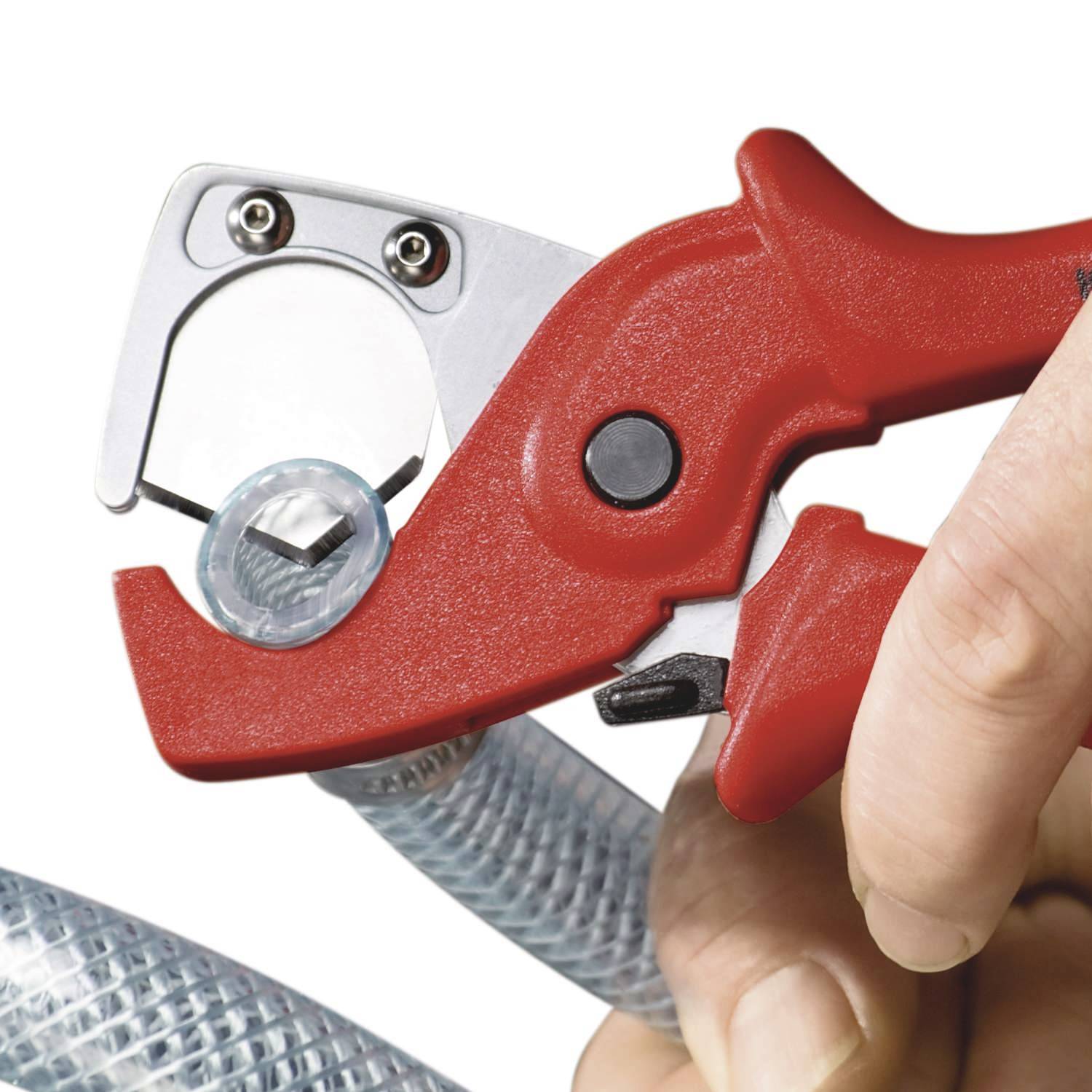 A red pipe cutter is cutting a flexible, transparent hose. A hand is holding the tool to guide the cut.