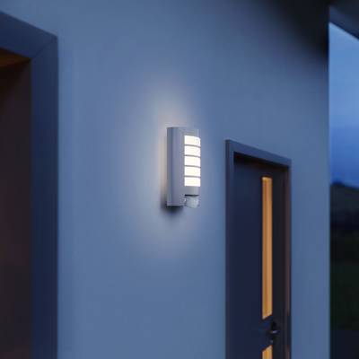 Exterior wall of a modern property with a wall light switched on beside a door; twilight atmosphere.