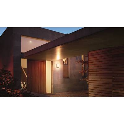 A modern house at dusk with exterior lighting switched on. The entrance door is made of wood, with the façade constructed from stone and wood.