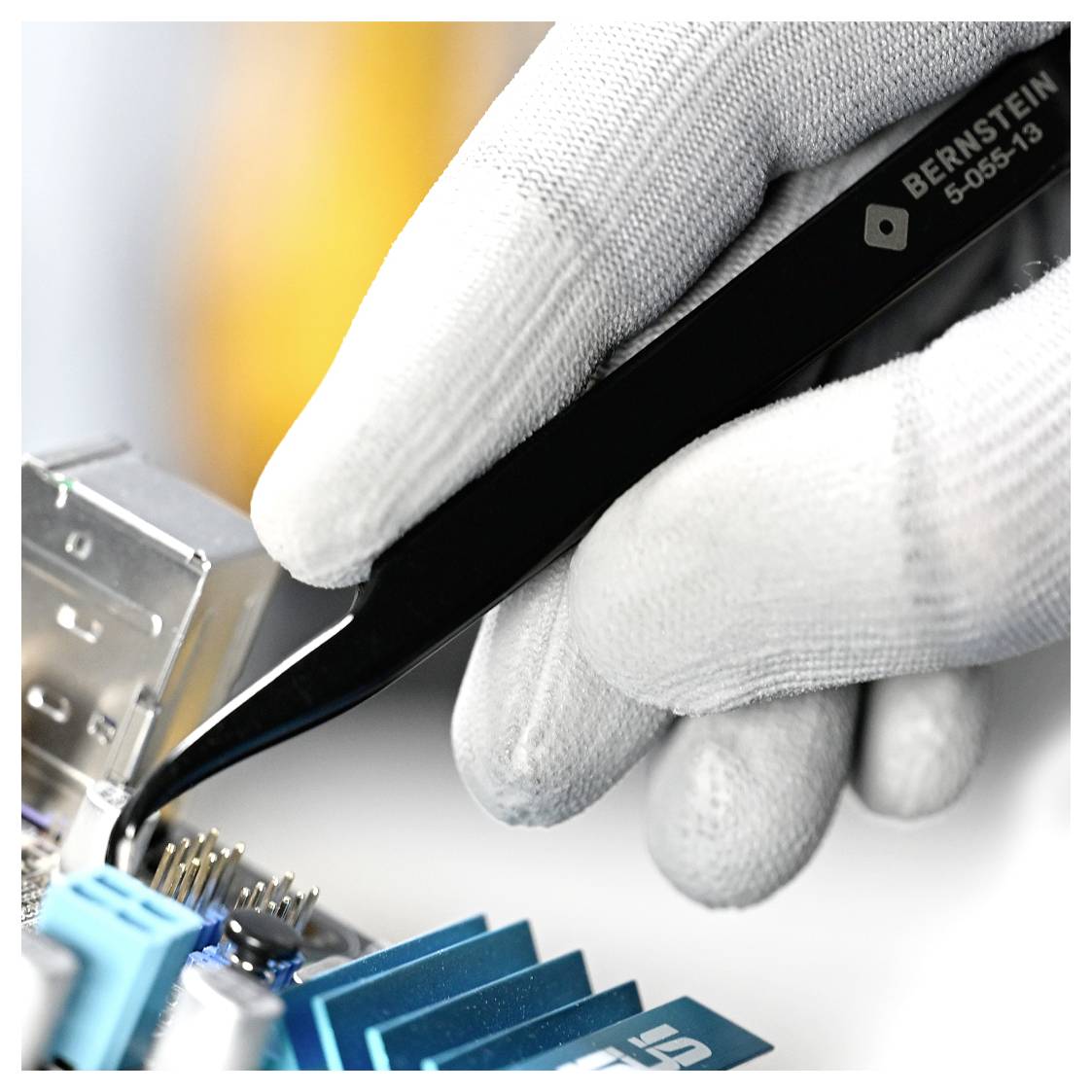 A gloved hand uses tweezers to adjust small components on a circuit board, indicating precise electronic work.