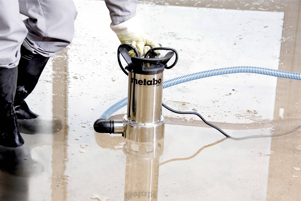 The person is using a pump to remove water from a flooded ground. The scene depicts flood protection measures.