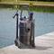 A black pond vacuum cleaner with attachments stands on a wooden deck by a pond. The pond and greenery are visible in the background.