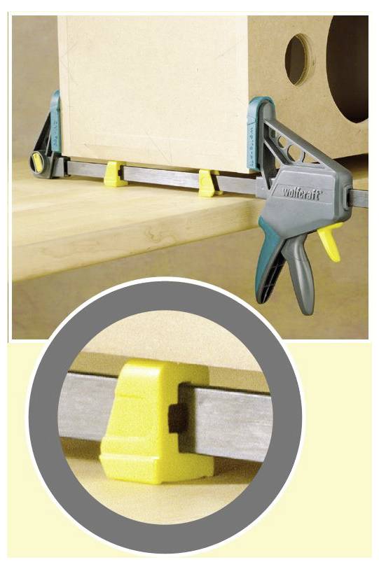 A lightweight clamp securing a wooden box to a tabletop, with a close-up showing a yellow plastic bracket on the clamp's metal bar.