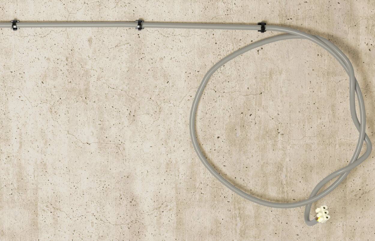 Grey spiral cable mounted on a bracket on a wall, coiled in a loop beside it on a light, textured background.