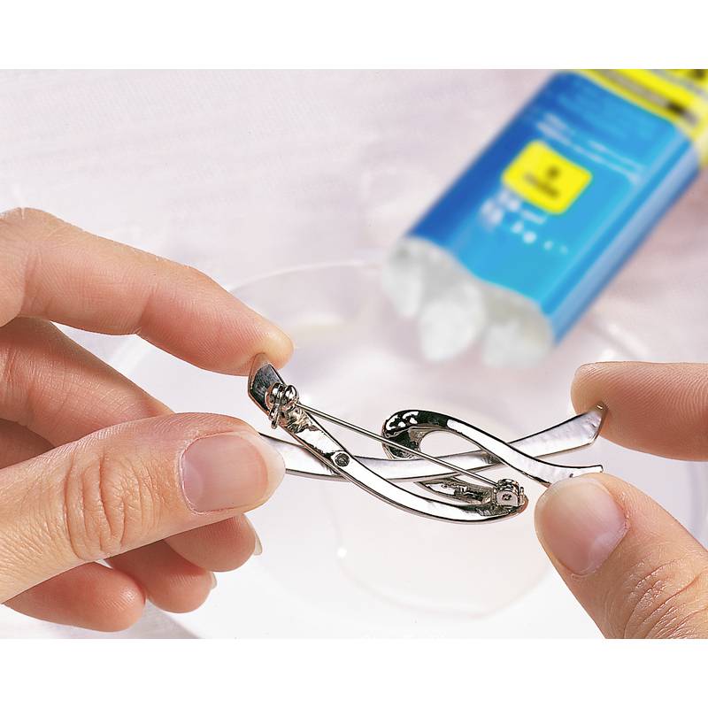 Two hands are holding an eyelash curler over a dish, with a blurry blue tube in the background.