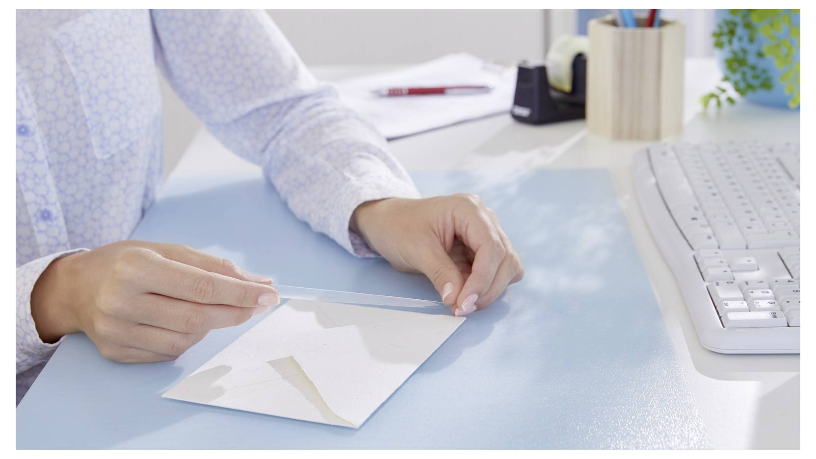 A person sealing an envelope at a desk with a computer keyboard, notebook, and pen in the background.