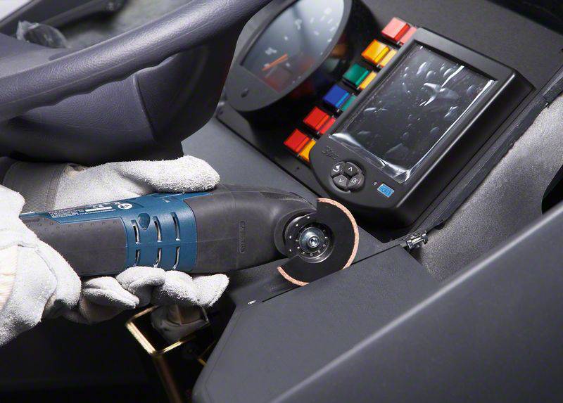 A gloved worker is adjusting a dashboard with an electric tool inside a vehicle to make modifications.