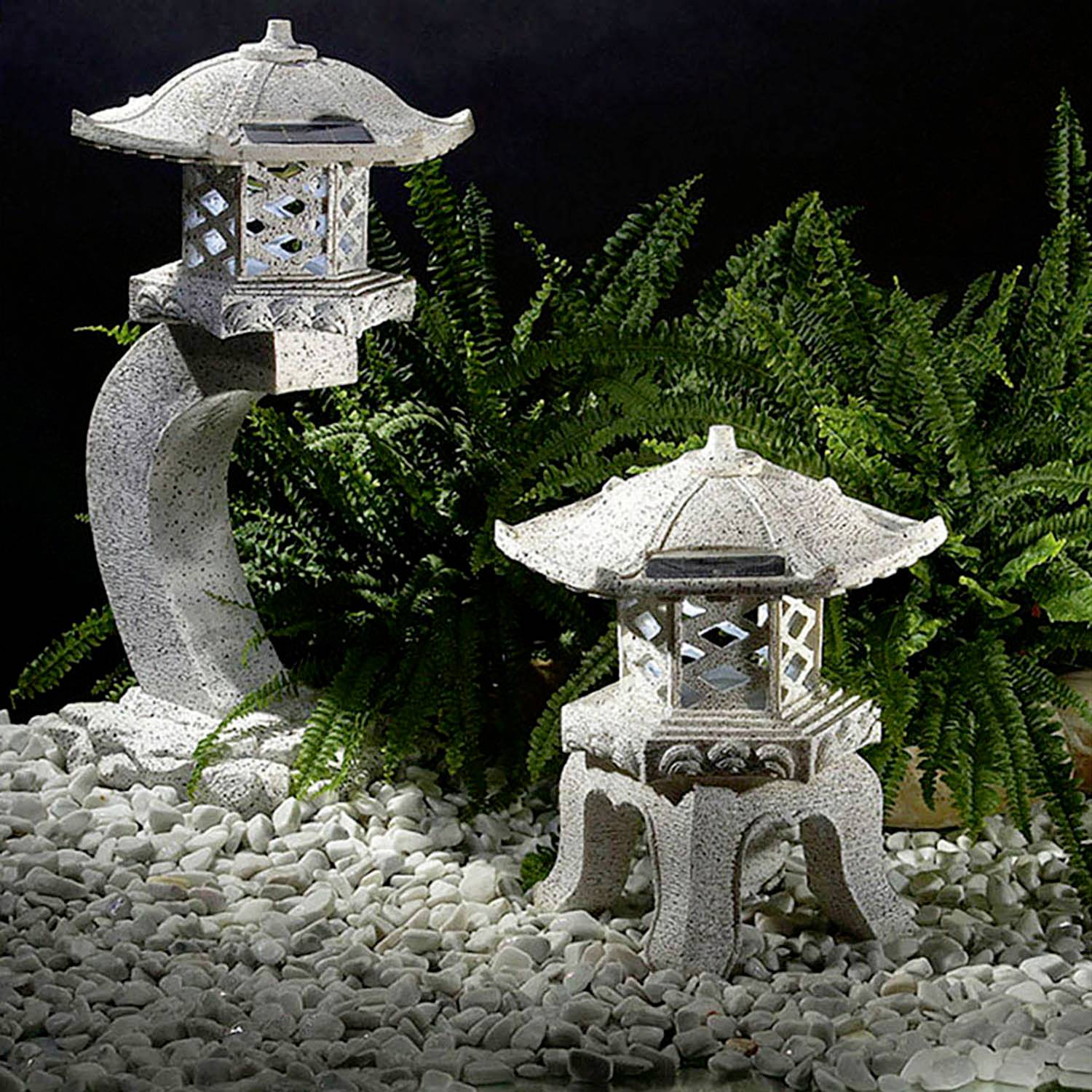 Two stone garden lanterns, one large and curved, the other small and simple, surrounded by green ferns and white pebbles.