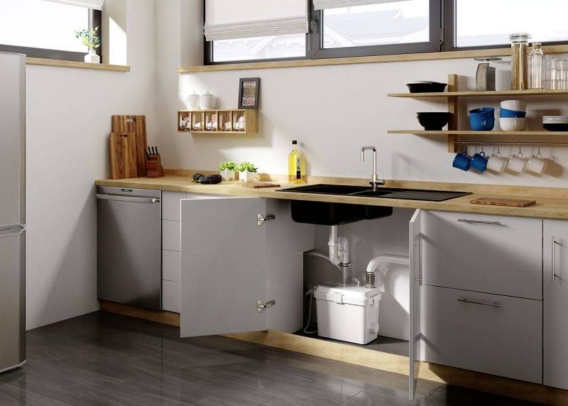 Modern kitchen with light wooden accents, open shelving beneath the sink and appliances on the worktop. Windows bring natural light into the space.