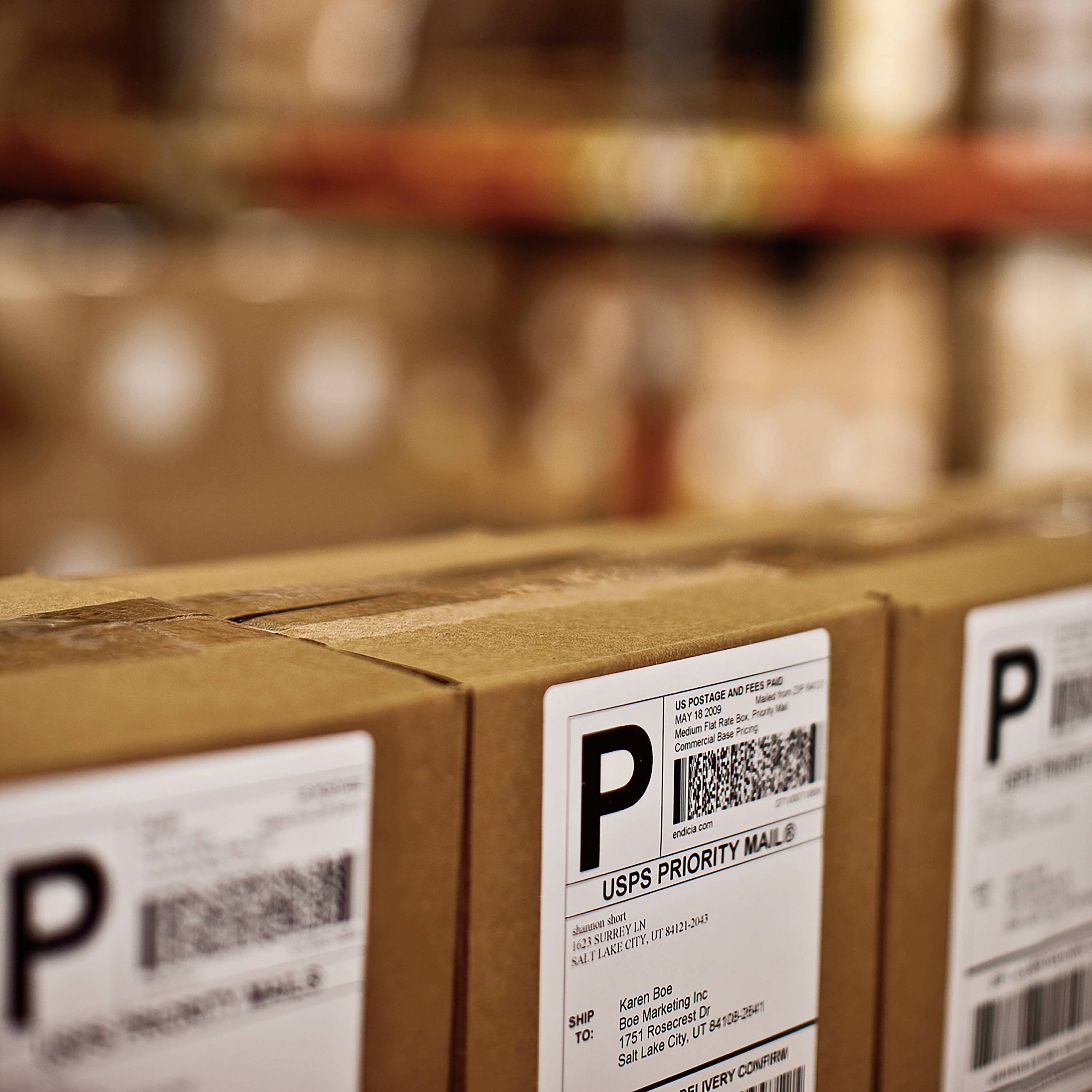 Packages with shipping labels on a warehouse shelf, ready for dispatch. Label includes barcode and address information.